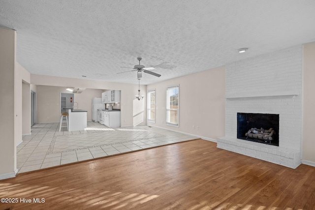 unfurnished living room with a textured ceiling, a fireplace, a ceiling fan, baseboards, and light wood-type flooring