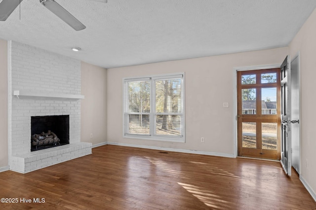 unfurnished living room with a brick fireplace, a textured ceiling, baseboards, and wood finished floors