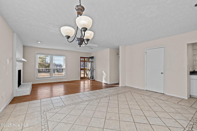 unfurnished living room featuring a textured ceiling, light tile patterned floors, a brick fireplace, and baseboards