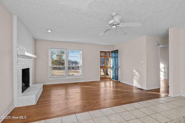 unfurnished living room with light wood finished floors, a barn door, ceiling fan, a textured ceiling, and a brick fireplace