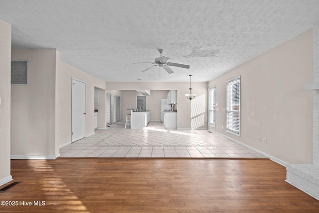 unfurnished living room featuring light wood finished floors, visible vents, and ceiling fan with notable chandelier