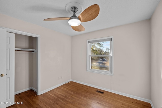 unfurnished bedroom featuring baseboards, a closet, visible vents, and wood finished floors