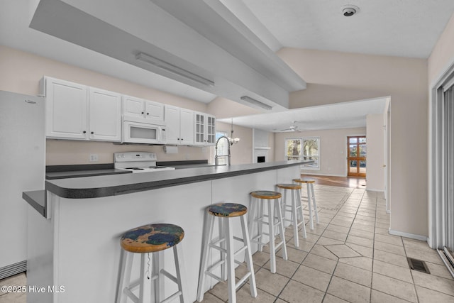 kitchen with a breakfast bar area, white appliances, white cabinetry, open floor plan, and dark countertops