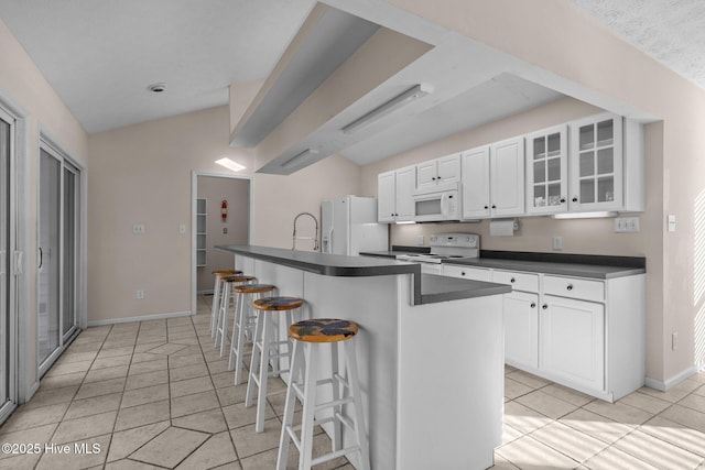 kitchen with a breakfast bar area, white appliances, white cabinetry, dark countertops, and glass insert cabinets