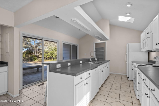 kitchen featuring dark countertops, white appliances, vaulted ceiling with skylight, and a sink