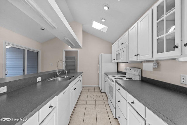 kitchen with dark countertops, lofted ceiling with skylight, white cabinetry, a sink, and white appliances