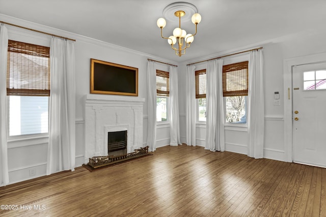unfurnished living room featuring hardwood / wood-style floors, crown molding, a notable chandelier, and a high end fireplace