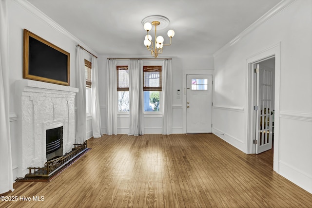 entrance foyer with wood-type flooring, a notable chandelier, a fireplace with raised hearth, and ornamental molding