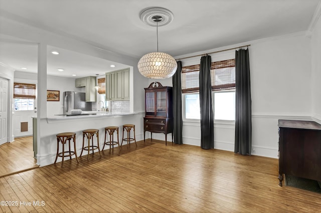 kitchen featuring light wood finished floors, tasteful backsplash, a breakfast bar, a peninsula, and freestanding refrigerator