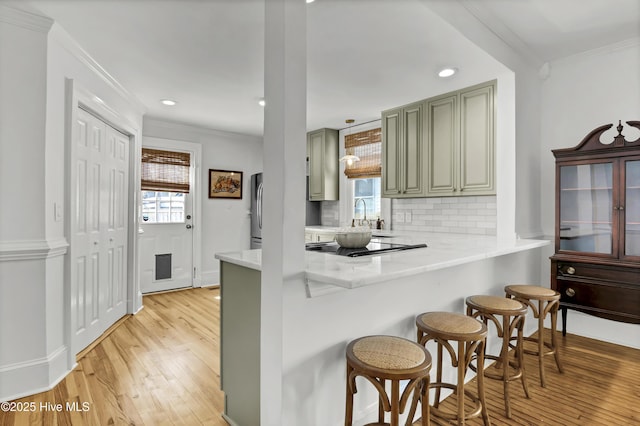 kitchen featuring a peninsula, light wood-style floors, a kitchen bar, crown molding, and tasteful backsplash