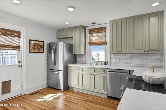 kitchen with light wood finished floors, backsplash, light countertops, stainless steel appliances, and a sink