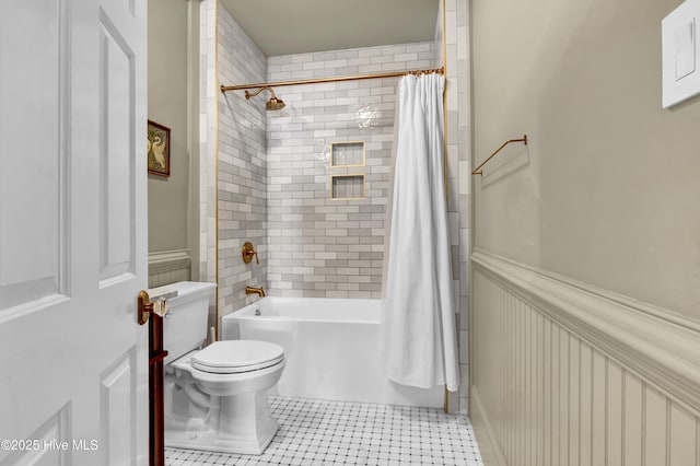bathroom featuring shower / bathtub combination with curtain, toilet, and wainscoting