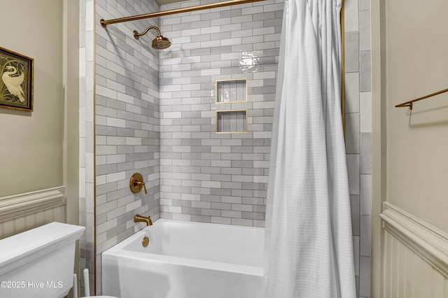 bathroom featuring toilet, shower / bathtub combination with curtain, and wainscoting