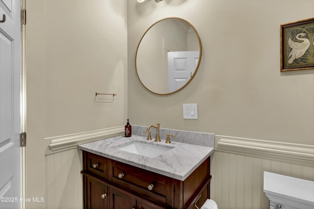 bathroom featuring a wainscoted wall, toilet, and vanity