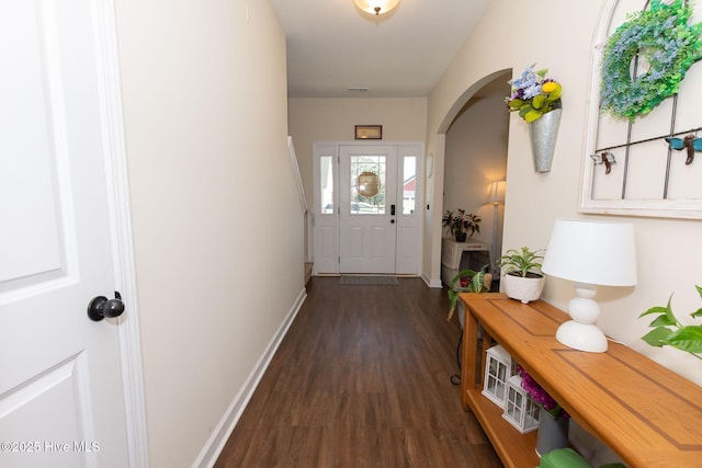 doorway with arched walkways, dark wood-style flooring, visible vents, and baseboards