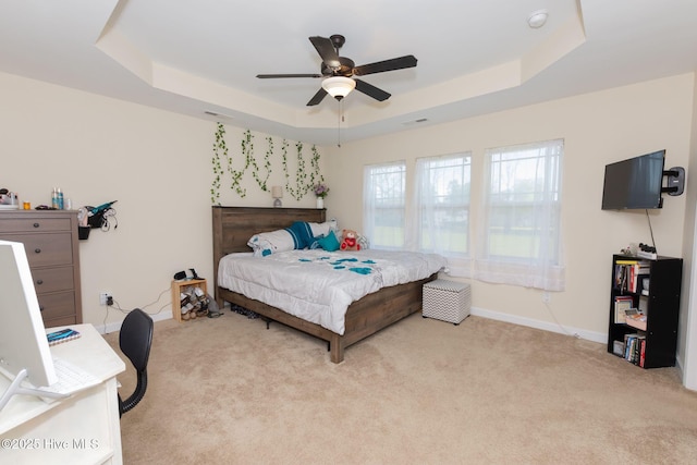 bedroom featuring baseboards, a tray ceiling, a ceiling fan, and light colored carpet