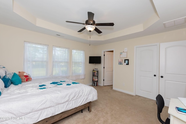 bedroom with baseboards, visible vents, a raised ceiling, and light colored carpet