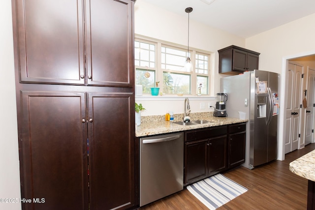 kitchen with dark wood-style flooring, pendant lighting, stainless steel appliances, a sink, and light stone countertops