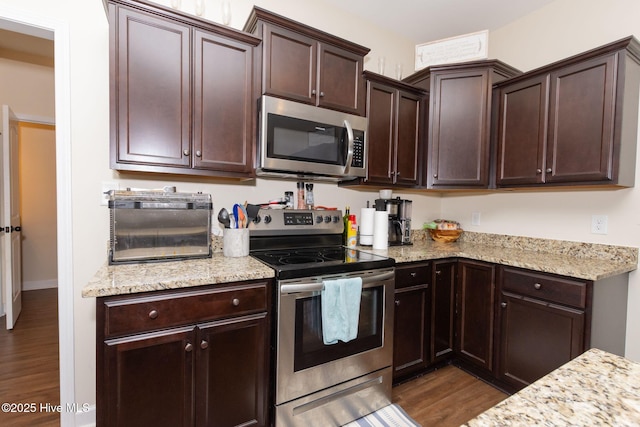 kitchen featuring appliances with stainless steel finishes, light stone countertops, dark brown cabinetry, and wood finished floors