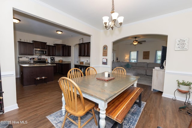 dining room with arched walkways, ceiling fan with notable chandelier, dark wood-style flooring, baseboards, and ornamental molding