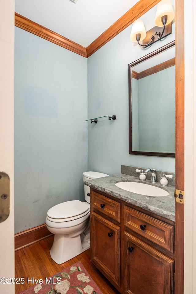 bathroom featuring toilet, ornamental molding, vanity, wood finished floors, and baseboards