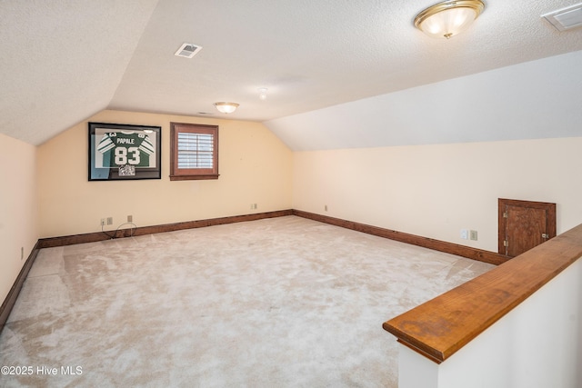 bonus room with lofted ceiling, visible vents, a textured ceiling, and baseboards