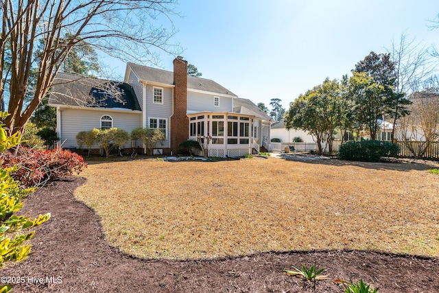 rear view of house featuring a sunroom, fence, a chimney, and a lawn