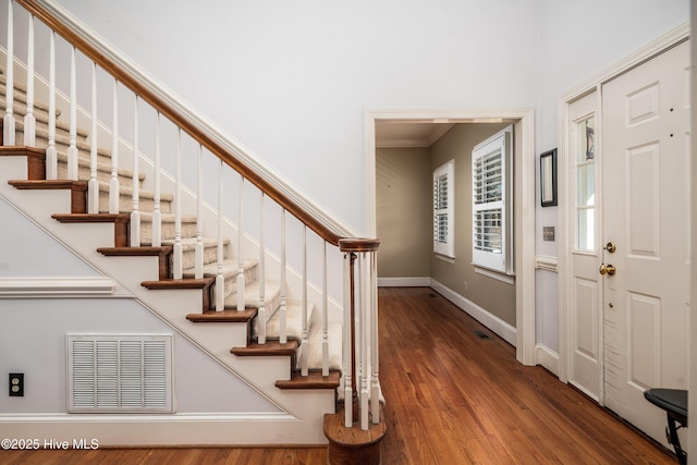 foyer entrance with visible vents, crown molding, baseboards, and wood finished floors