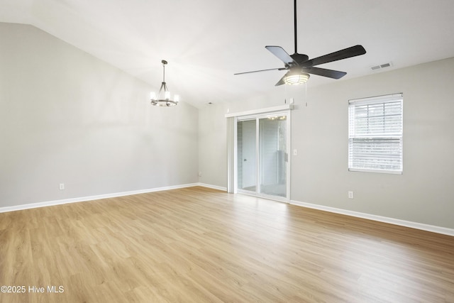 empty room with visible vents, ceiling fan with notable chandelier, baseboards, light wood finished floors, and lofted ceiling