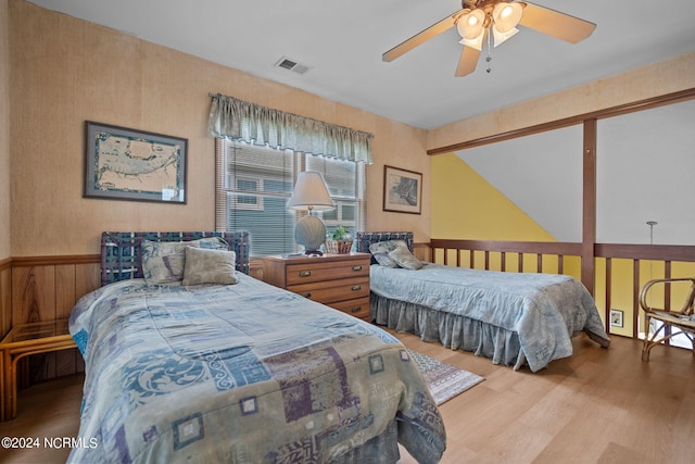 bedroom featuring a wainscoted wall, a ceiling fan, visible vents, and wood finished floors