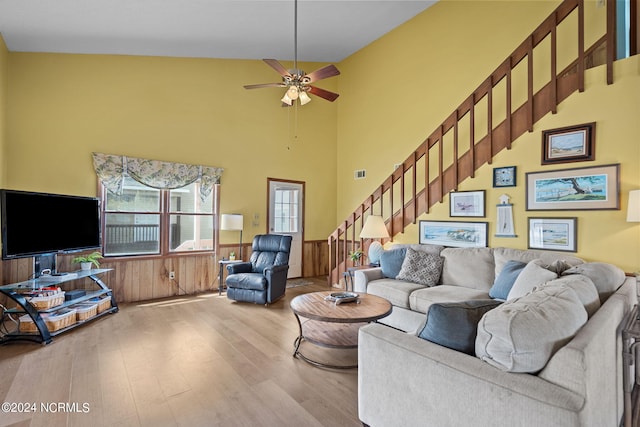 living area with a wainscoted wall, wood walls, wood finished floors, a ceiling fan, and stairs