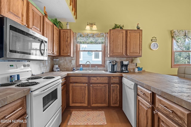 kitchen with white appliances, decorative backsplash, brown cabinets, light wood-type flooring, and a sink