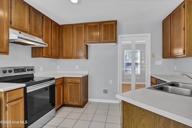 kitchen featuring brown cabinets, stainless steel electric range, light countertops, under cabinet range hood, and a sink