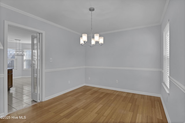 unfurnished room featuring crown molding, light wood finished floors, baseboards, and a notable chandelier