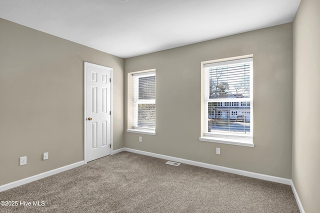 carpeted spare room featuring visible vents, a wealth of natural light, and baseboards