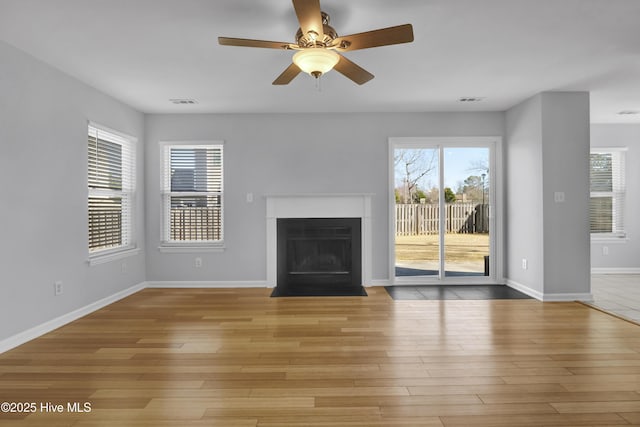 unfurnished living room featuring a healthy amount of sunlight, light wood-style floors, a fireplace with flush hearth, and baseboards