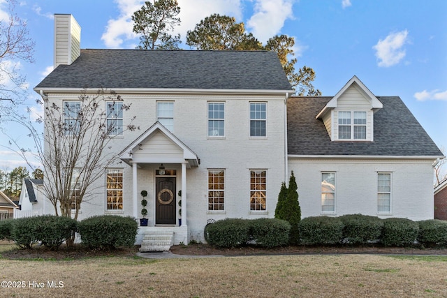 view of front facade with brick siding, a front yard, and a shingled roof