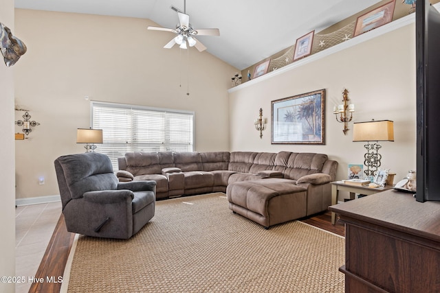 living room with a ceiling fan, light wood-style floors, baseboards, and high vaulted ceiling