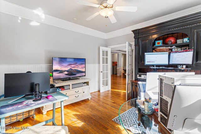 home office with french doors, crown molding, a ceiling fan, wainscoting, and wood finished floors