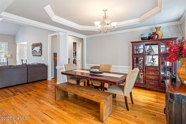 dining space with light wood finished floors, wainscoting, ornamental molding, an inviting chandelier, and a tray ceiling