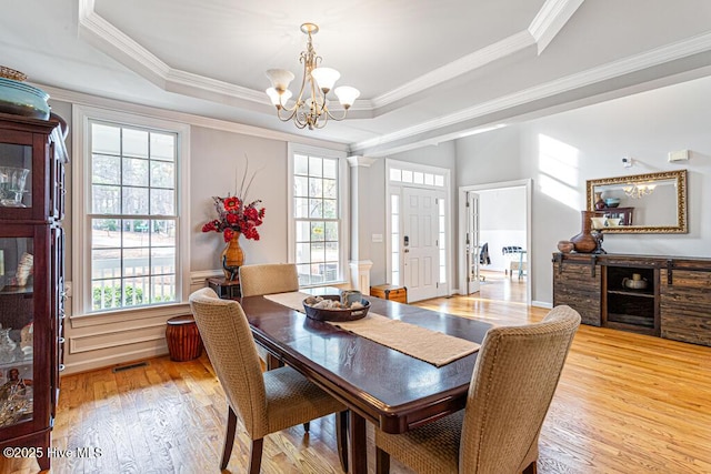 dining space featuring light wood-style floors, a raised ceiling, and plenty of natural light