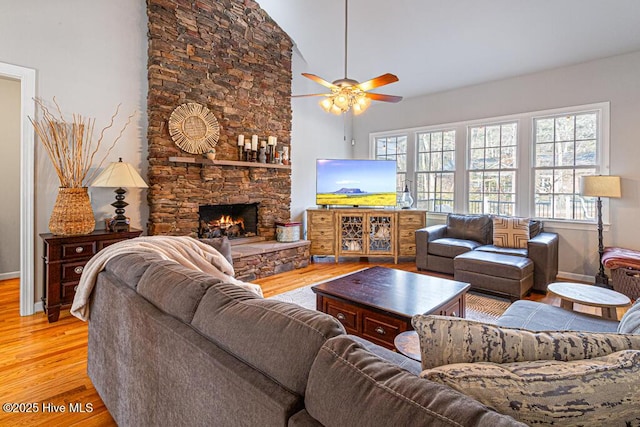 living room featuring a ceiling fan, a fireplace, light wood-style flooring, and baseboards