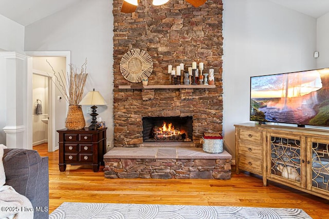 living room with vaulted ceiling, a stone fireplace, and wood finished floors