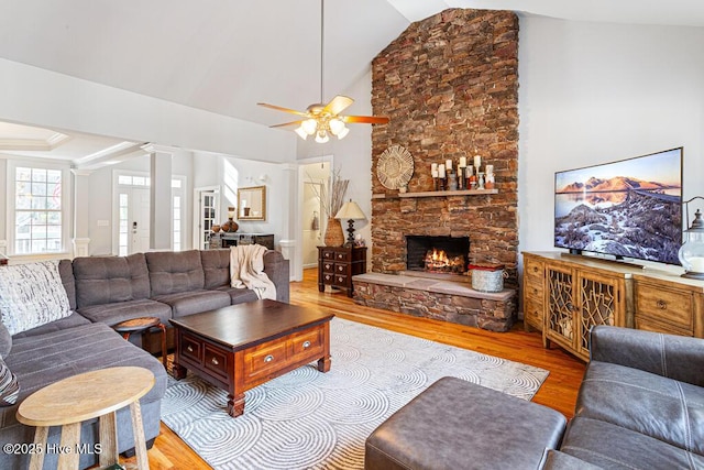 living area featuring ornate columns, high vaulted ceiling, wood finished floors, and a stone fireplace