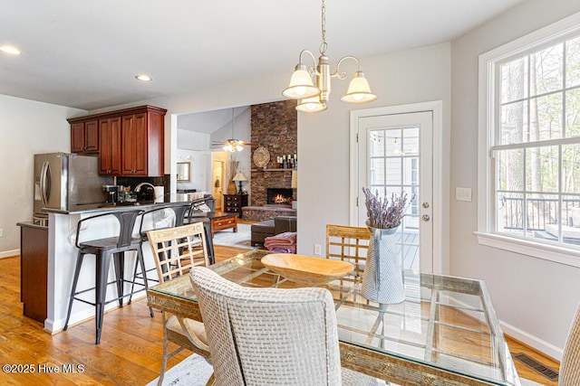 dining space featuring light wood-style flooring, a wealth of natural light, and a stone fireplace