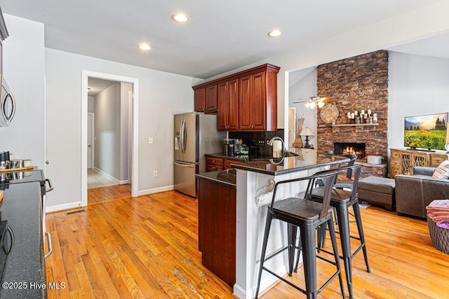 kitchen with light wood-type flooring, stainless steel appliances, a stone fireplace, and a kitchen breakfast bar