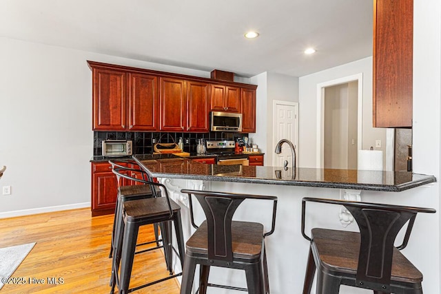 kitchen with light wood finished floors, backsplash, appliances with stainless steel finishes, dark brown cabinets, and a kitchen bar