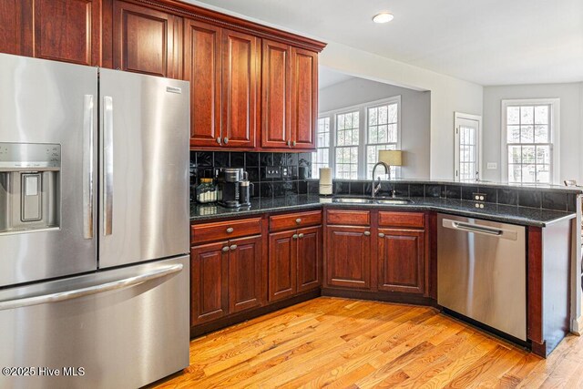 kitchen with tasteful backsplash, appliances with stainless steel finishes, light wood-style floors, a sink, and a peninsula