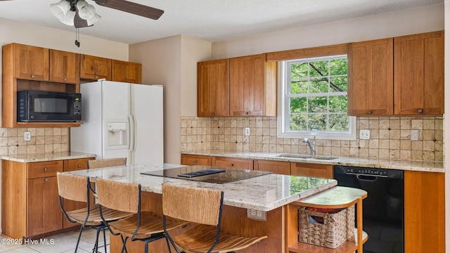 kitchen with brown cabinets, a sink, a kitchen breakfast bar, decorative backsplash, and black appliances