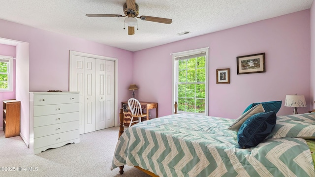 bedroom with a ceiling fan, a textured ceiling, visible vents, carpet floors, and a closet